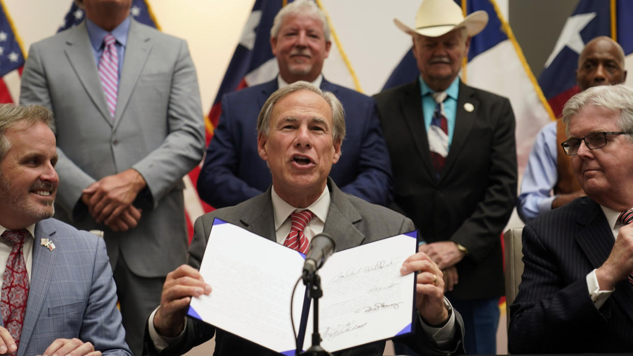 Texas Gov. Greg Abbott shows off his signature after signing Senate Bill 1, also known as the election integrity bill, into law in Tyler, Texas, on Tuesday. He is flanked by State Sen. Bryan Hughes, R-Mineola, front center left, and Lieutenant Gov. Dan Patrick, front right.