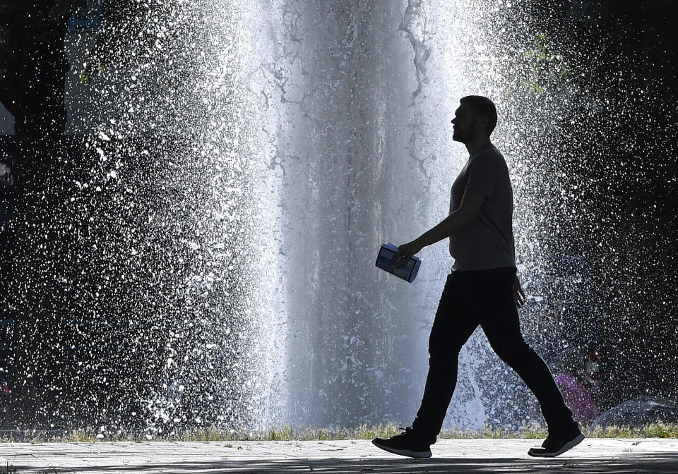 A man passes a fountain on an extreme hot summer day, with highs of 40 degrees Celsius, Wednesday, July 24, 2019 in the center of Gelsenkirchen, Germany. Europe faces another heatwave with record temperatures. (AP Photo/Martin Meissner)