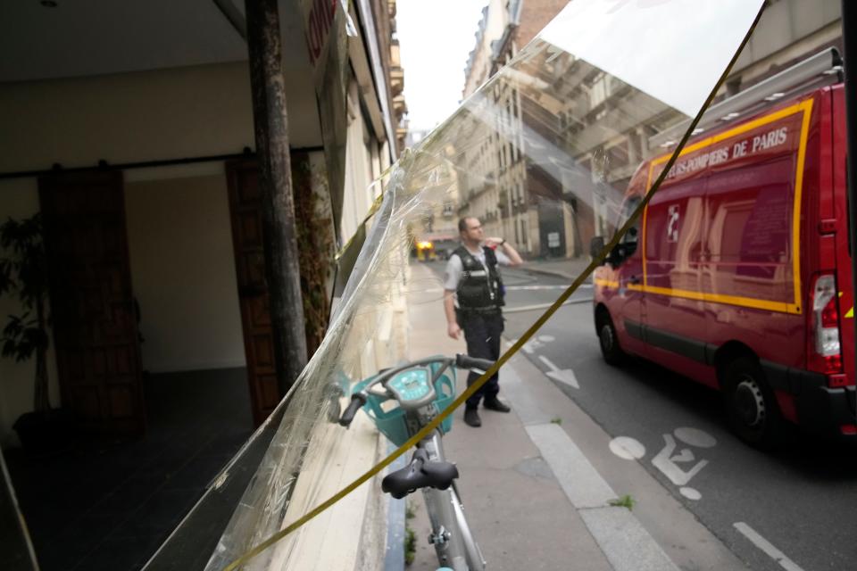 A police officer stands by damaged window as a rescue vehicle drives to a blaze Wednesday, June 21, 2023 in Paris. Firefighters fought a blaze on Paris' Left Bank that is sent smoke soaring over the domed Pantheon monument and prompted evacuation of buildings in the neighborhood, police said. Local media cited witnesses describing a large explosion preceding the fire, and saying that part of a building collapsed.