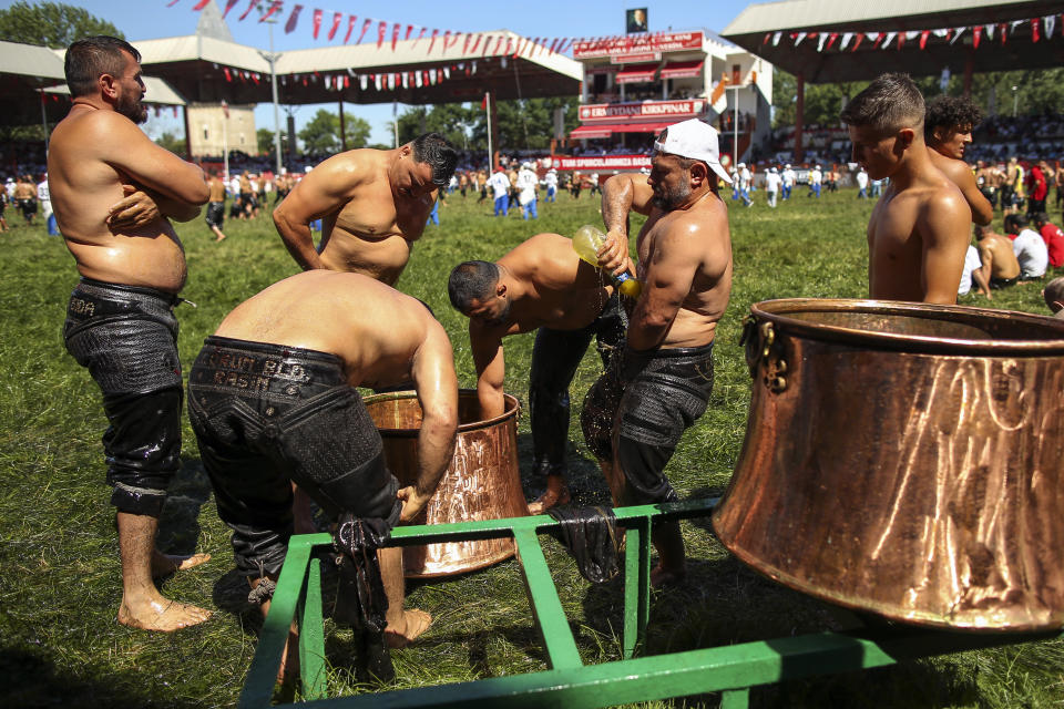 An 'oiler', someone charged with oiling up wrestlers and filling up oil pitchers, douses wrestlers in olive oil, during the 660th instalment of the annual Historic Kirkpinar Oil Wrestling championship, in Edirne, northwestern Turkey, Saturday, July 10, 2021.Thousands of Turkish wrestling fans flocked to the country's Greek border province to watch the championship of the sport that dates to the 14th century, after last year's contest was cancelled due to the coronavirus pandemic. The festival, one of the world's oldest wrestling events, was listed as an intangible cultural heritage event by UNESCO in 2010. (AP Photo/Emrah Gurel)