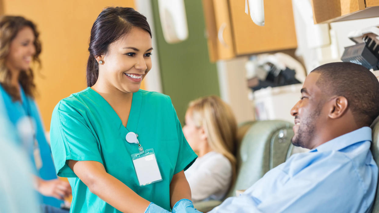 Happy nurse comforting patient while he donates blood to hospital.