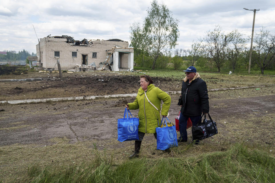 People walk with their belongings to the evacuation point in front of a building that was damaged by a Russian airstrike in Vilcha, near Vovchansk, Ukraine, Sunday, May 12, 2024. (AP Photo/Evgeniy Maloletka)