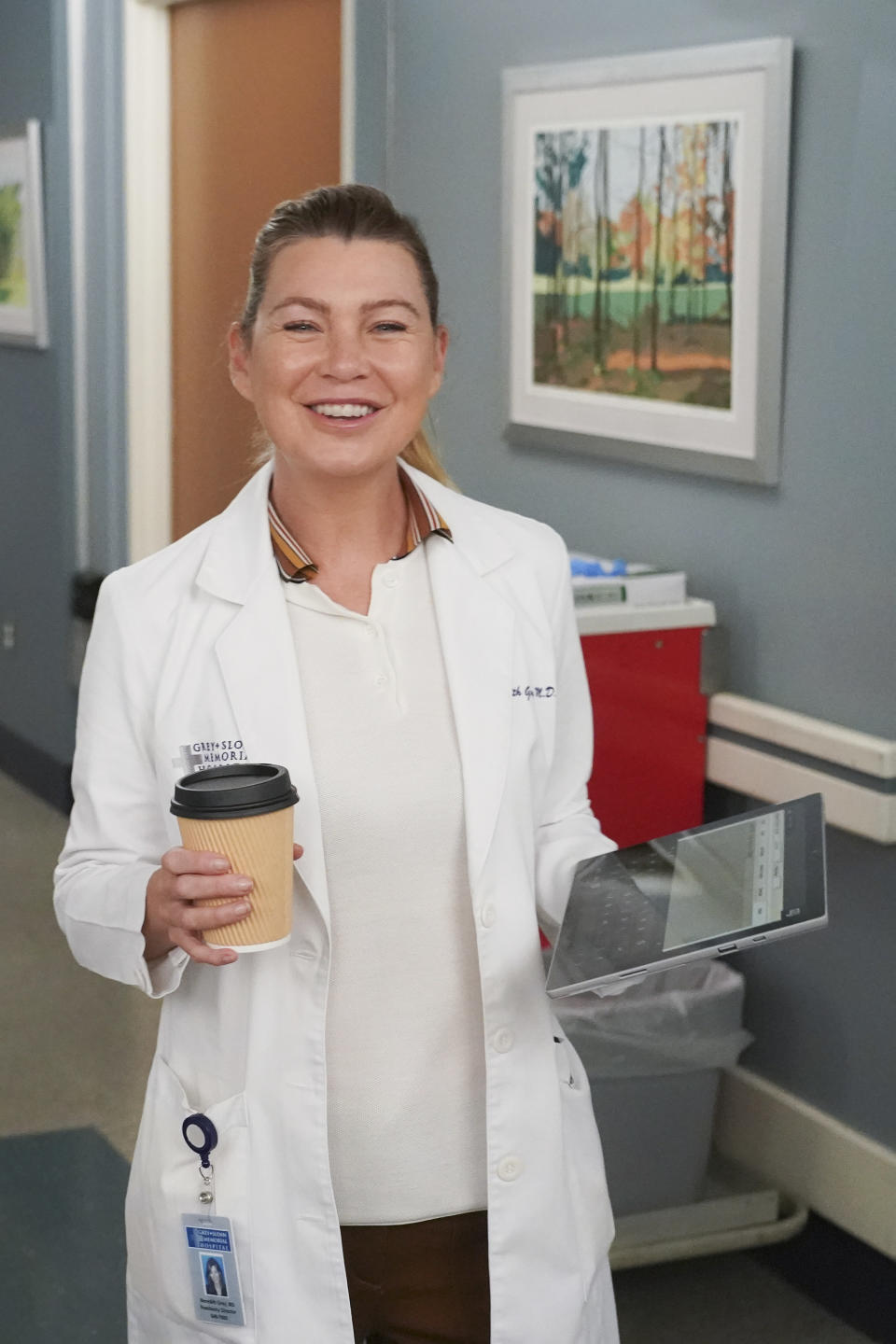 ellen in character in her doctor's coat holding a tablet and a coffee