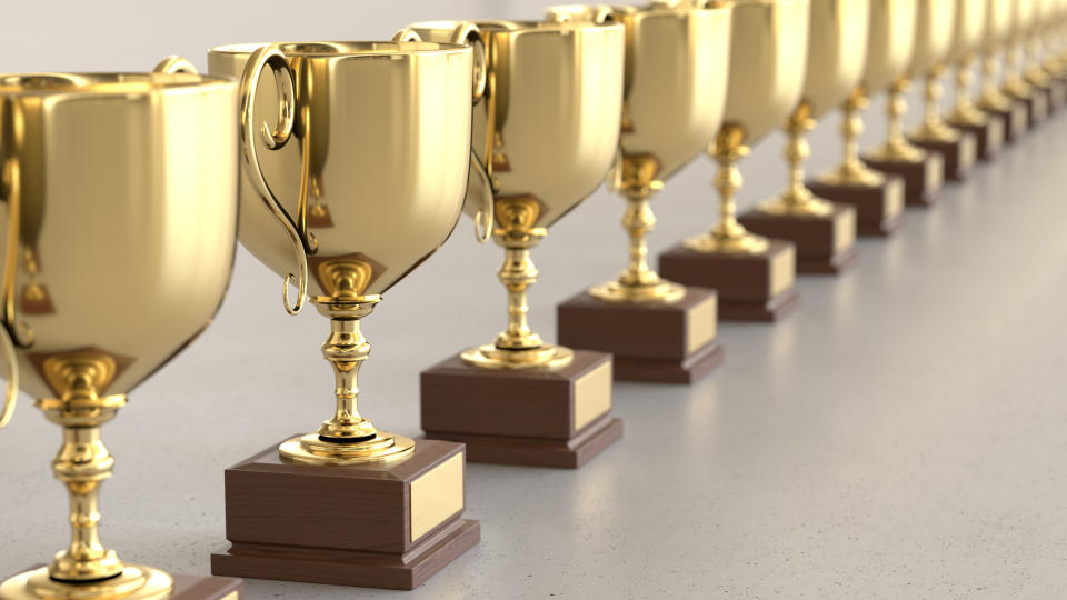 A row of gold trophies on a grey table.