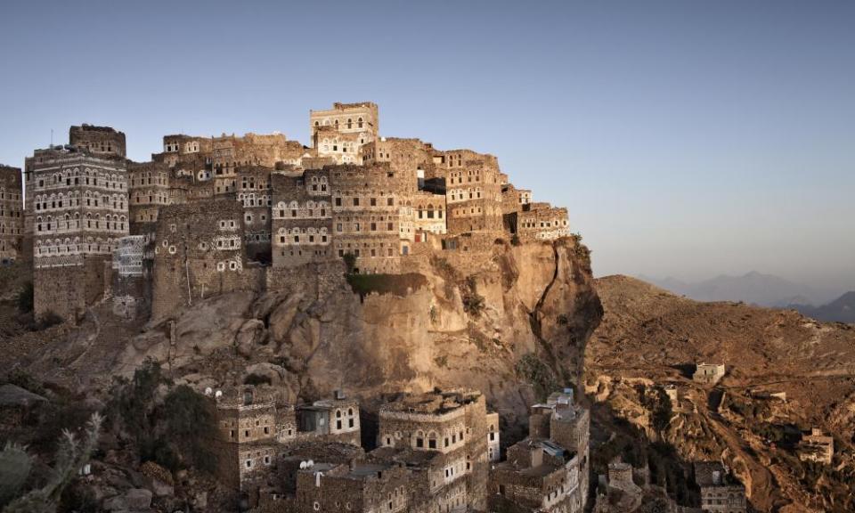 A striking series of stone buildings perched on top of a crag, with the peaks of other mountains visible in the haze behind