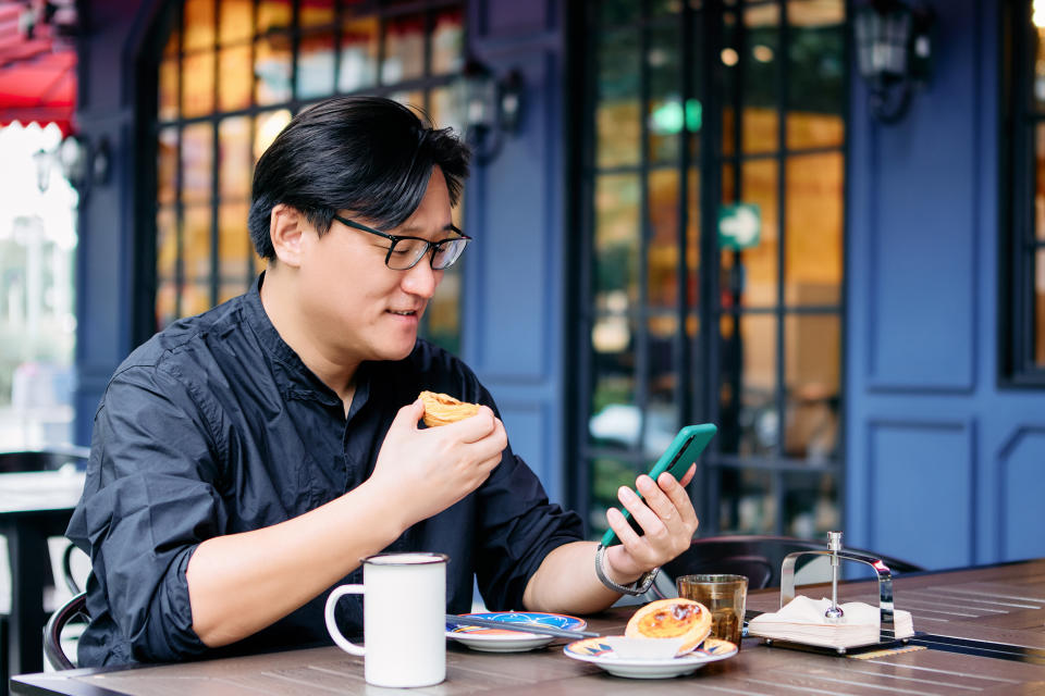 Asian man eating egg tart in outdoor restaurant