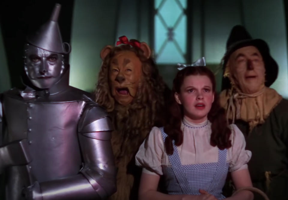 Tin Man, Cowardly Lion, Dorothy, and Scarecrow gaping at someone offscreen