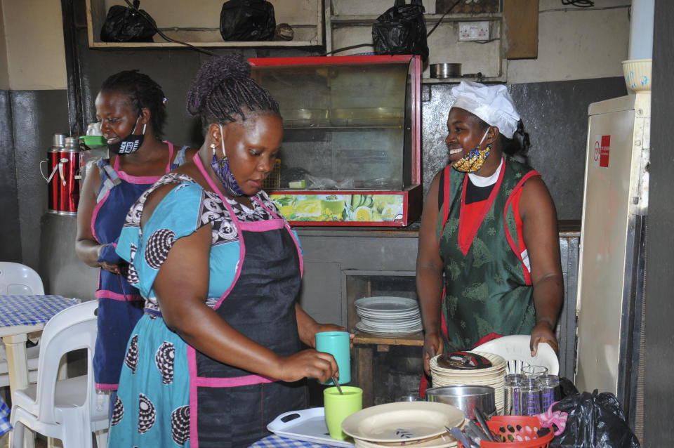 In this photo taken Saturday, June 20, 2020, Rebecca Nakamanya, right, and colleague Namara Grace, center, work at a restaurant near a bus terminal in capital Kampala, Uganda. The COVID-19 pandemic means that millions of women in Africa and other developing regions could lose years of success in contributing to household incomes, asserting their independence and expanding financial inclusion. (AP Photo/Ronald Kabuubi)