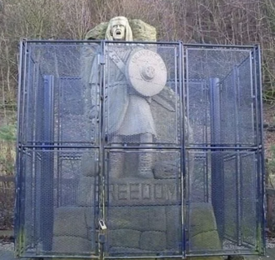 Statue of a figure with a shield and sword trapped behind a metal cage, with the word "FREEDOM" at the base