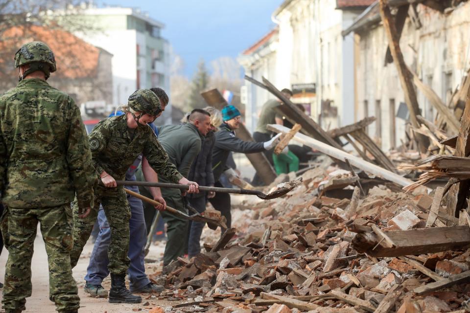 Croatian soldiers and people clean rubble next to damaged buildings in Petrinja, some 50kms from Zagreb, after the town was hit by an earthquake of the magnitude of 6,4 on December 29, 2020. - The tremor, one of the strongest to rock Croatia in recent years, collapsed rooftops in Petrinja, home to some 20,000 people, and left the streets strewn with bricks and other debris. Rescue workers and the army were deployed to search for trapped residents, as a girl was reported dead. (Photo by Damir SENCAR / AFP) (Photo by DAMIR SENCAR/AFP via Getty Images)