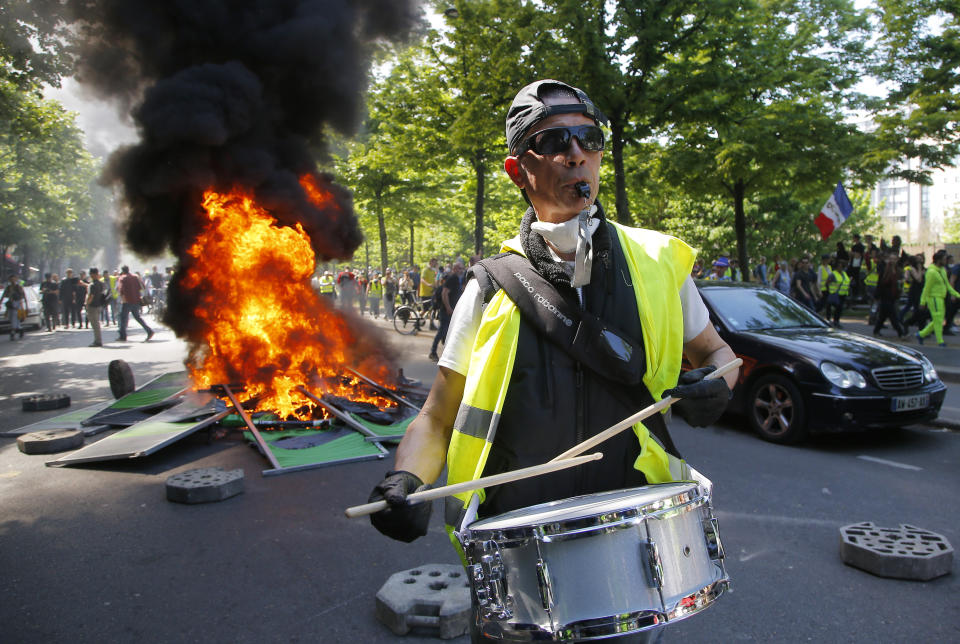 A man bangs a drum in front of a fire on the street during a yellow vest demonstration in Paris, Saturday, April 20, 2019. French yellow vest protesters are marching anew to remind the government that rebuilding the fire-ravaged Notre Dame Cathedral isn't the only problem the nation needs to solve. (AP Photo/Michel Euler)