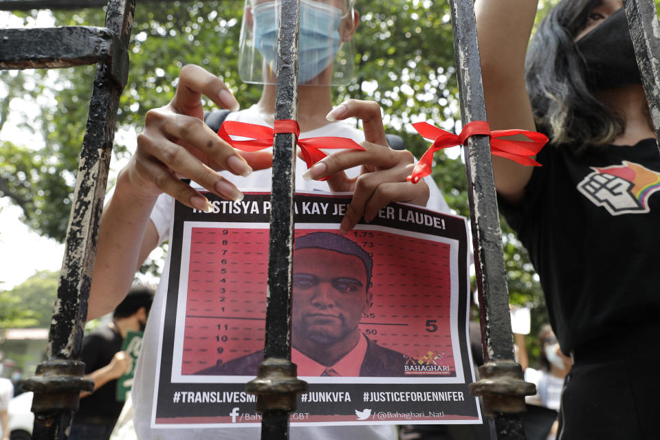 A demonstrator ties a red ribbon on a gate of the Department of Justice to symbolize their protest while holding a picture of U.S. Marine Lance Cpl. Joseph Scott Pemberton during a rally in Manila, Philippines on Thursday, Sept. 3, 2020. A Philippine court has ordered the early release for good conduct of Pemberton convicted in the 2014 killing of a transgender Filipino which sparked anger in the former American colony. (AP Photo/Aaron Favila)