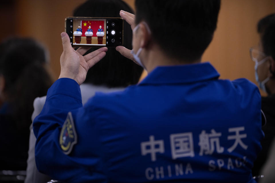 A staff member takes a smartphone photo of Chinese astronauts for the upcoming Shenzhou-16 mission, from left, Gui Haichao, Jing Haipeng, and Zhu Yangzhu as they stand behind glass during a meeting of the press at the Jiuquan Satellite Launch Center in northwest China on Monday, May 29, 2023. China's space program plans to land astronauts on the moon before 2030, a top official with the country's space program said Monday. (AP Photo/Mark Schiefelbein)