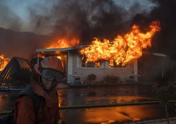 A firefighter turns away from the heat as flames explode through the front windows of a home burning in the Lilac fire.