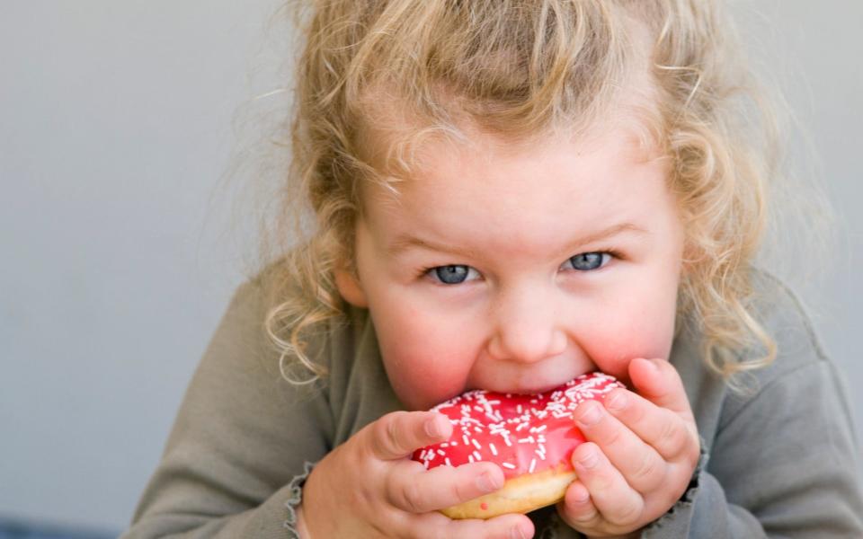 Young girl eating doughnut - Getty Images Contributor