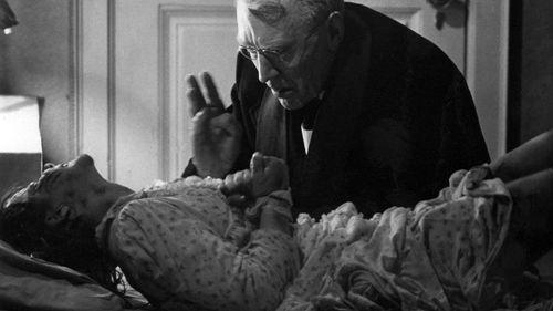 a priest sits over the bed of a possessed girl in a scene from the exorcist a good housekeeping pick for best halloween movies