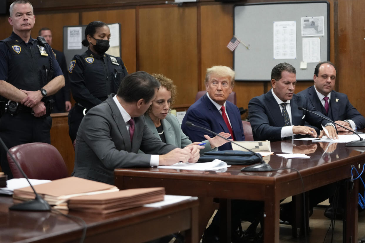 Former President Donald Trump sits in court for his arraignment, surrounded by his lawyers.