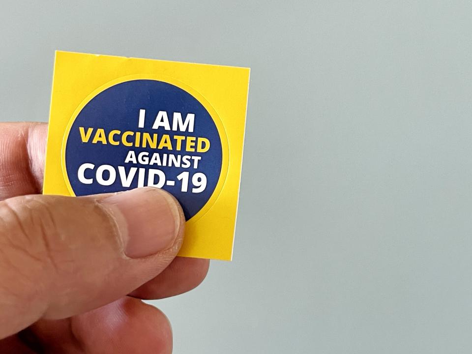 Man holding a sticker that says, "I Am Vaccinated Against COVID-19"