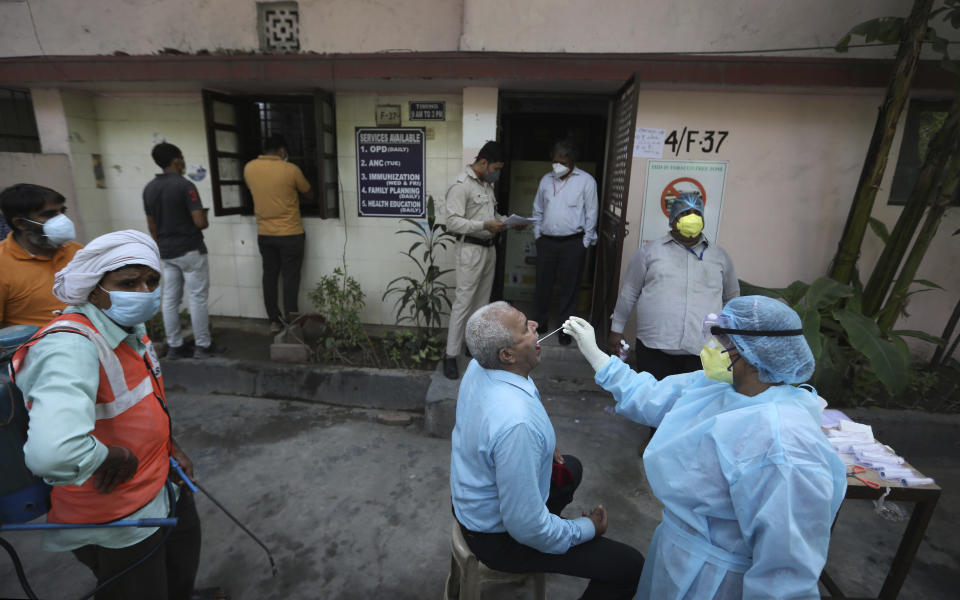 FILE- In this June 10, 2020 file photo, a health worker takes a swab of an elderly man for COVID-19 test in New Delhi, India. India is expanding its COVID-19 vaccination drive beyond health care and front-line workers, offering the shots to older people and those with medical conditions that put them at risk.(AP Photo/Manish Swarup, File)