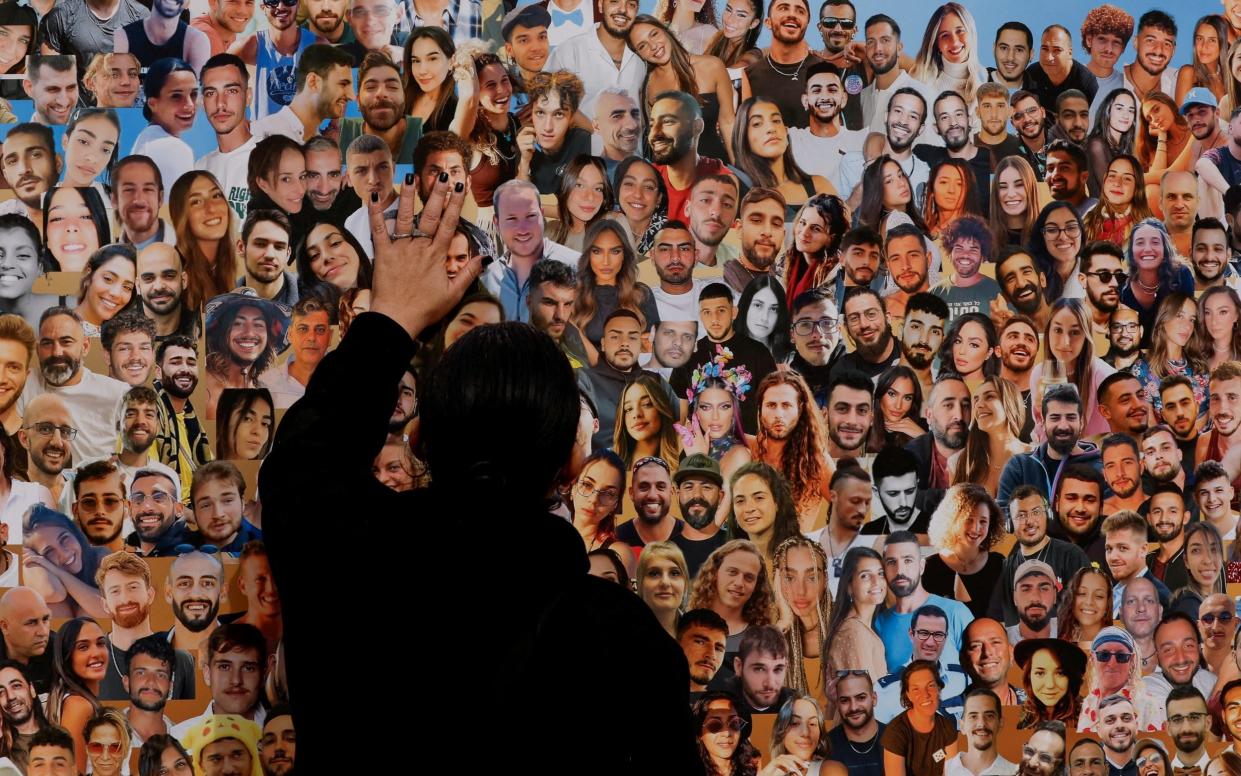 An Israeli pays tribute to a wall of photos of people killed and kidnapped on Oct 7