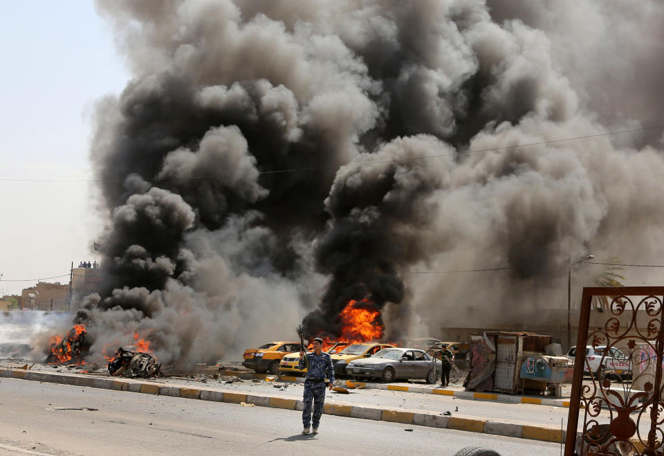 Iraqi policemen stand near burning vehicles moments after one in a series of bombs hit the Shiite stronghold of Sadr City, in Baghdad, Iraq, Tuesday, May 13, 2014. A wave of car bombings in mainly Shiite areas of Baghdad killed tens on Tuesday, officials said. (AP Photo/Karim Kadim)