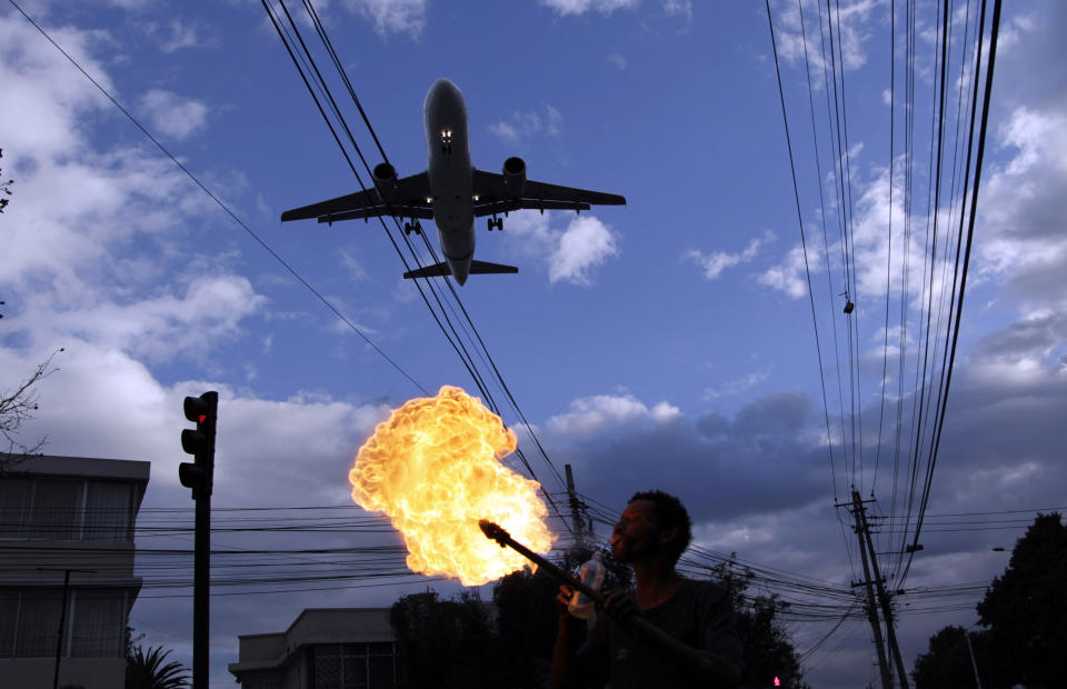 In this Jan. 22, 2013 photo, a plane approaches the Mariscal Sucre airport for landing over a fire spitting street performer in Quito, Ecuador. There are a lot more people living near the airport than when it opened in 1960. Just about 350,000 lived in Quito then. The population has grown to about 2.2 million now. Quito is moving its airport to an agricultural setting 12 miles (20 kilometers) northeast of the city, joining other cities that have moved, or tried to move, planes further from people. (AP Photo/Dolores Ochoa)