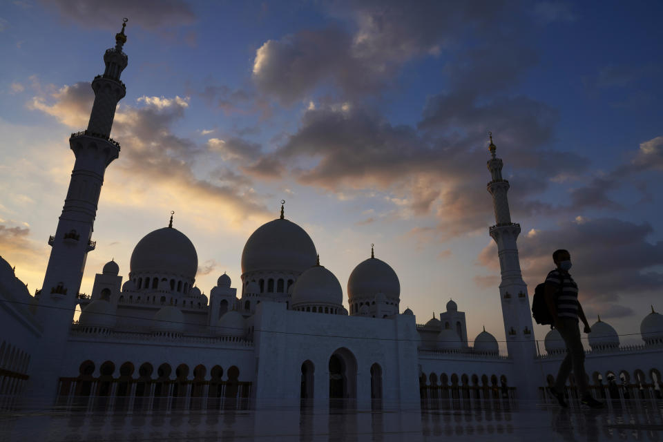A tourist walks through Sheikh Zayed Grand Mosque at dusk in Abu Dhabi, United Arab Emirates, Wednesday, Dec. 9, 2020. Abu Dhabi announced Wednesday it would resume "all economic, tourism, cultural and entertainment activities in the emirate within two weeks." It attributed the decision to "successes" in halting the spread of the coronavirus. (AP Photo/Jon Gambrell)