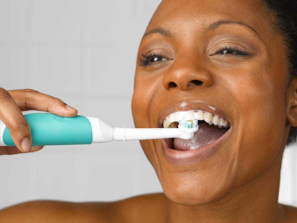 woman brushing teeth with electronic toothbrush