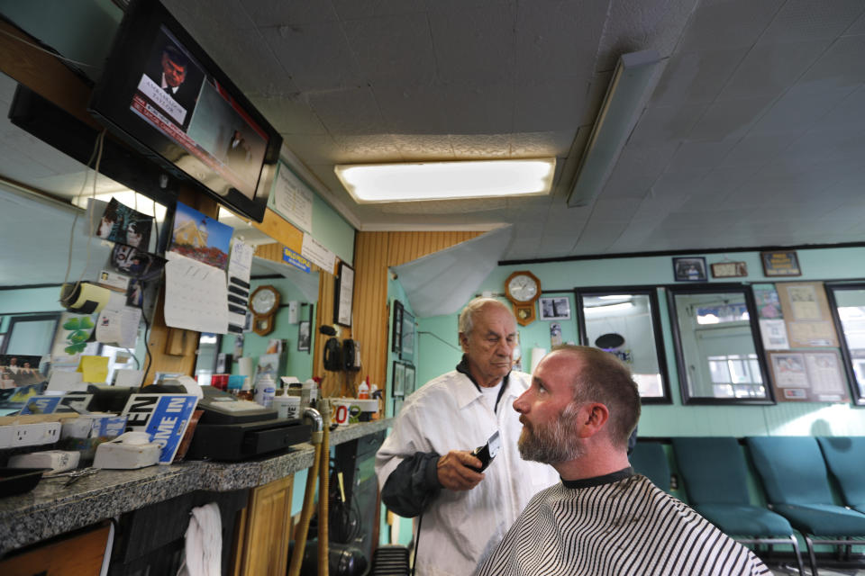 Seth Morrill glances up at a TV monitor televising the impeachment hearings while getting his hair cut, Wednesday, Nov. 13, 2019, in Portland, Maine. Morrill said the hearing are very important but he would not intentionally carve time out of his day to watch them, saying he would catch up on the news later, via the internet. (AP Photo/Robert F. Bukaty)