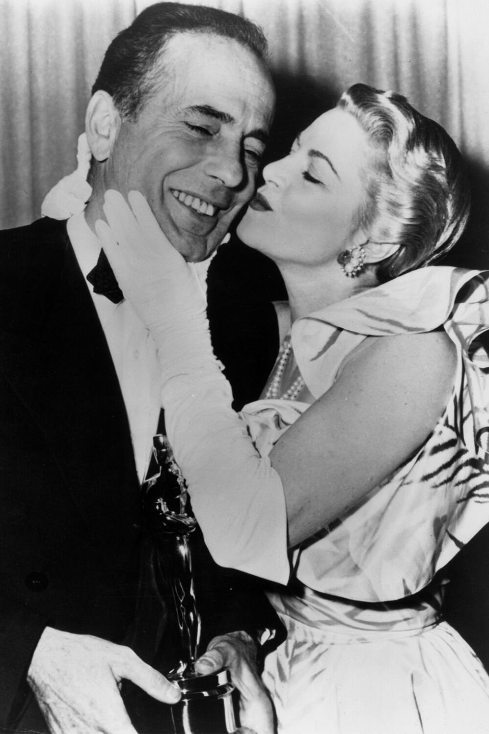 1952: American actor Humphrey Bogart (1899-1957) receives a kiss from actor Claire Trevor (1909 - 2000) while standing backstage with the Best Actor Oscar he won for his role in director John Huston's film, 'The African Queen,' RKO Pantages Theatre, Los Angeles, California. (Photo by Hulton Archive/Getty Images)