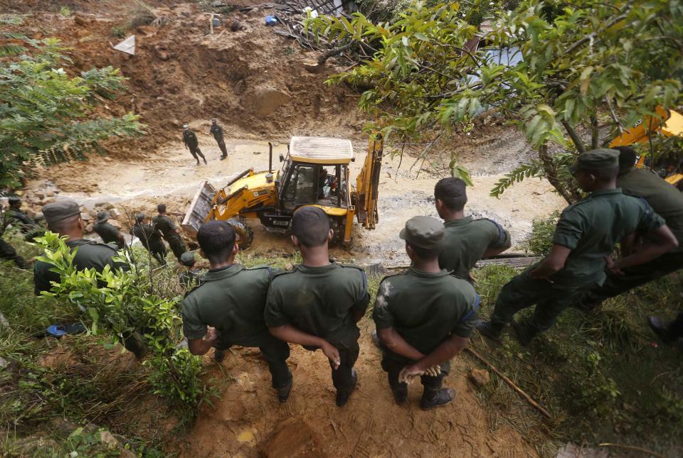 Members of a military rescue team watch as heavy equipment is used to clear debris at the site of a landslide at the Koslanda tea plantation near Haldummulla