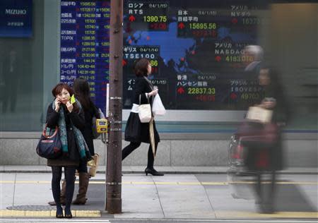 Pedestrians stand in front of a stock quotation board displaying stock prices outside a brokerage in Tokyo January 15, 2014. REUTERS/Yuya Shino