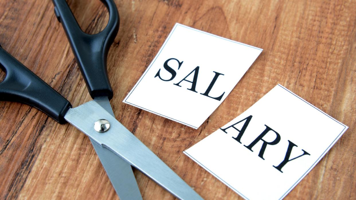  Scissors lying on a table next to a piece of paper that says "salary," cut in half. 