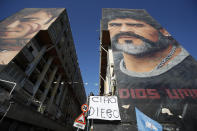 A woman hangs a sign with writing in Italian reading "Bye Diego" from a building showing a giant mural of soccer legend Diego Maradona, in Naples, southern Italy, Thursday, Nov. 26, 2020. Maradona died Wednesday, Nov. 25, 2020 in Buenos Aires. (AP Photo/Alessandra Tarantino)