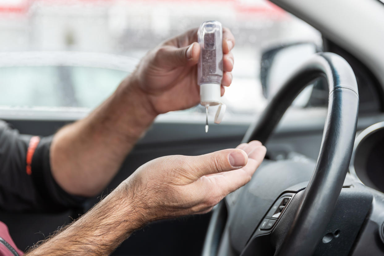 Man using hand sanitizer while sitting in car, he is cleaning her hands after shopping.