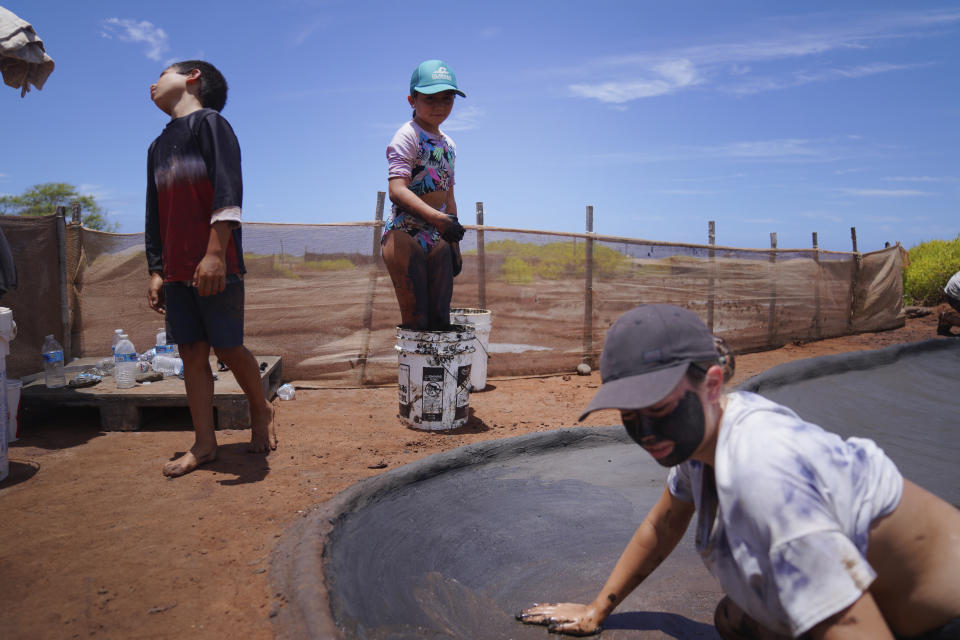 From left, siblings Kekanemekala Taniguchi Butler, Pi'ilani Taniguchi Butler, and Anali'a Taniguchi Butler use dark, wet clay to reconstruct salt beds used in making traditional Hawaiian salt on Wednesday, July 12, 2023, in Hanapepe, Hawaii. 22 Native Hawaiian families work the beds each summer to make "paakai," or Hawaiian salt, which can only be given away or traded, not sold. (AP Photo/Jessie Wardarski)