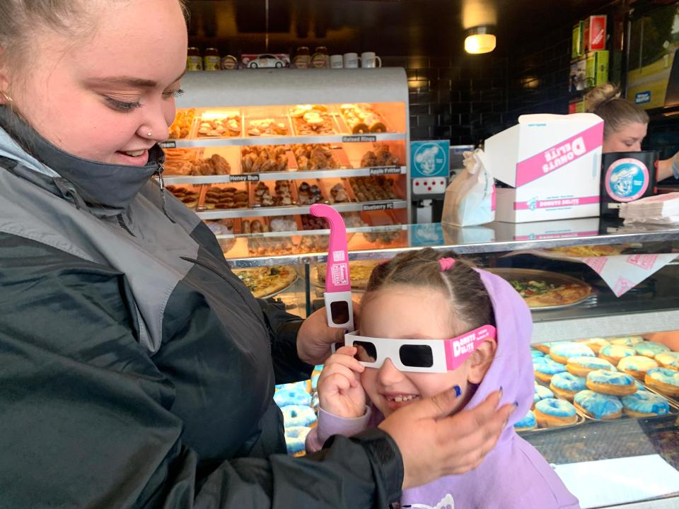 Brianna Casanova, left, of Rochester, helps her daughter Khani Casanova, 5, try on eclipse glasses at Donuts Delite on April 8, 2024.