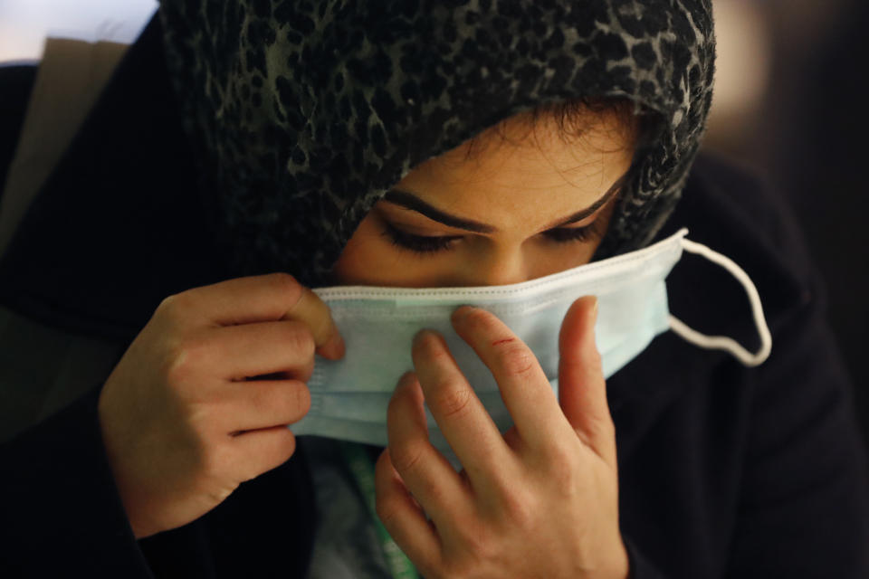 In this Wednesday, April 22, 2020, RUSH Hospital respiratory therapist Jumana Azam puts on a surgical mask after standing before a face temperature scanner as she reports for her early morning shift at the hospital in Chicago. (AP Photo/Charles Rex Arbogast)