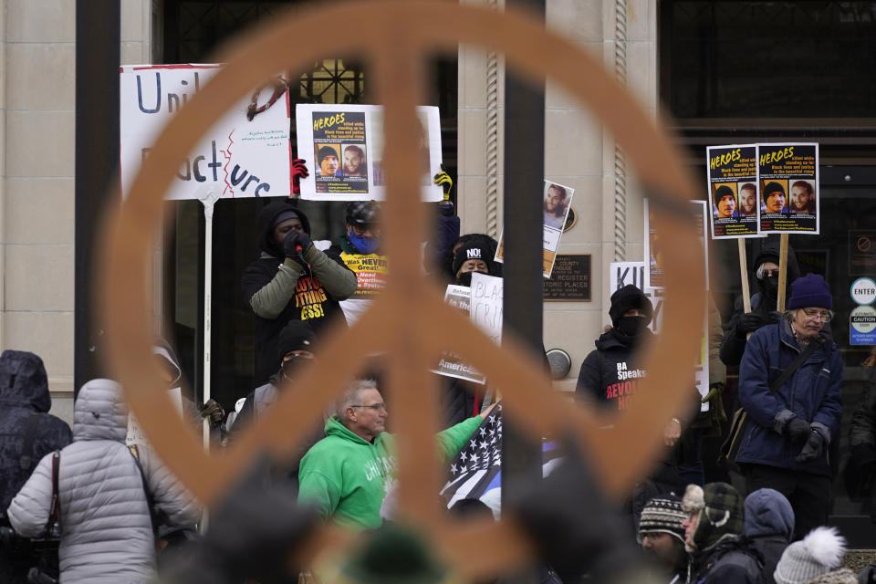 Protesters, framed by a peace symbol, stand outside the Kenosha County Courthouse, Thursday, Nov. 18, 2021 in Kenosha, Wis., during the Kyle Rittenhouse murder trial. Rittenhouse is accused of killing two people and wounding a third during a protest over police brutality in Kenosha last year. (AP Photo/Paul Sancya)