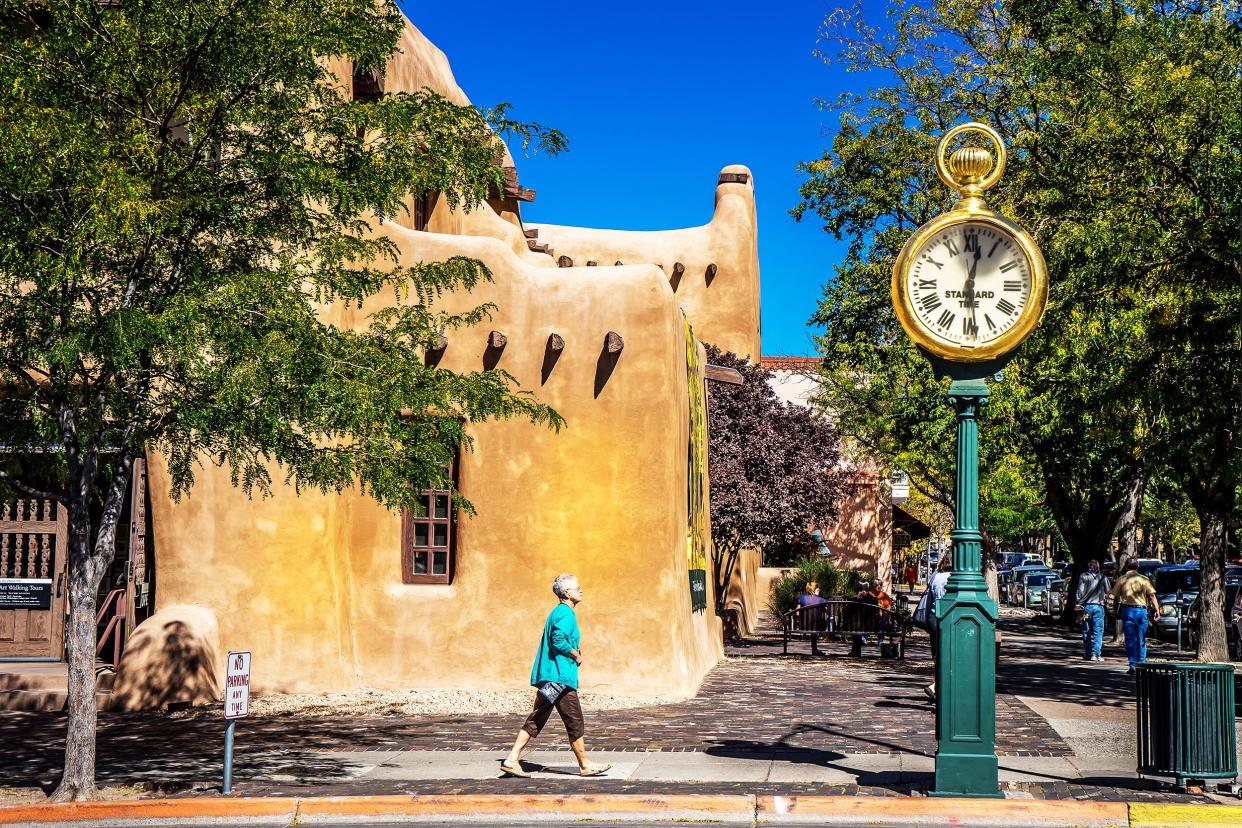 Native American Market, Santa Fe, New Mexico, woman wearing turquoise tunic walking along side walk near large clock