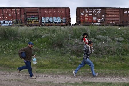 A Salvadoran father (R) carries his son while running next to another immigrant as they try to board a train heading to the Mexican-U.S. border, in Huehuetoca, near of Mexico City, June 1, 2015. REUTERS/Edgard Garrido/File Photo