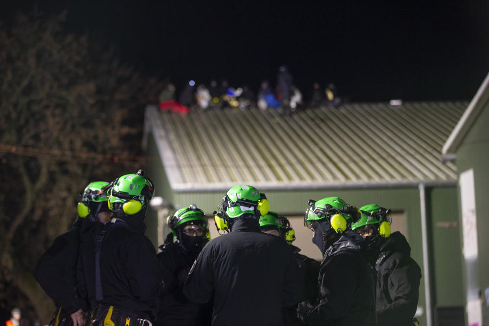 Climate activists sit on the roof of a barn, in the foreground high-altitude climbers of the police stand together for a situation briefing in Luetzerath, near Erkelenz, Germany, Wednesday, Jan. 11, 2023. Environmental activists have been locked in a standoff with police who started eviction operations on Wednesday around the hamlet of Luetzerath, west of Cologne, that’s due to be bulldozed for the expansion of a nearby lignite mine. (Thomas Banneyer/dpa via AP)