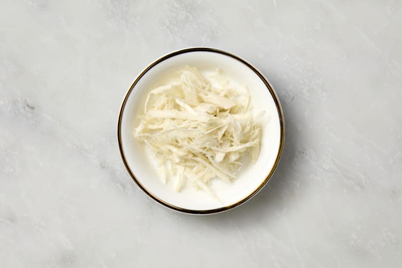 overhead shot of white horseradish on a small white plate with gold rim.