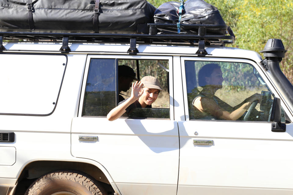 A child in a 4WD waves out the back passenger window while a woman drives. 