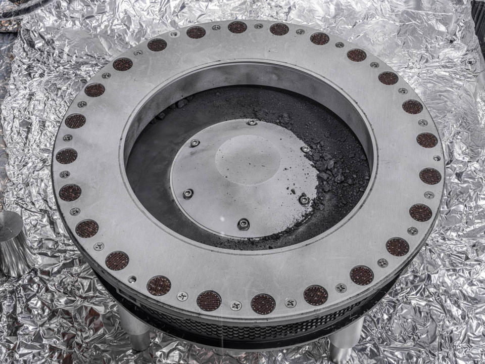 This photo provided by NASA on Wednesday, Oct. 11, 2023 shows the outside of the Osiris-Rex sample collector with material from asteroid Bennu at middle right. Scientists have found evidence of both carbon and water in initial analysis of this material. The bulk of the sample is located inside. (Erika Blumenfeld, Joseph Aebersold/NASA via AP