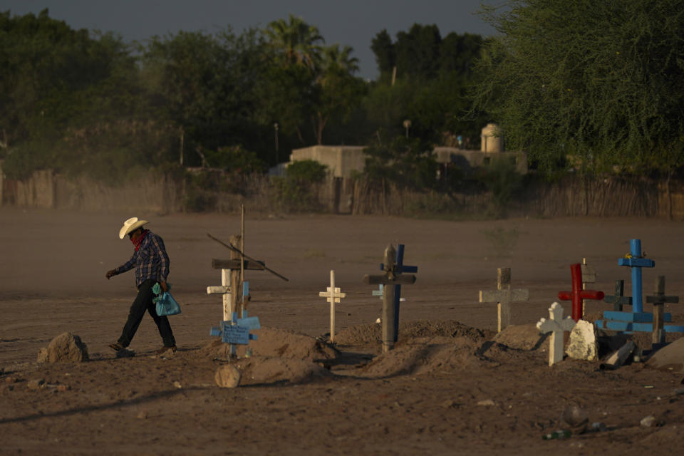 A Yaqui Indigenous wears a bandana over his mouth as he walks through dust past the cemetery where slain water-defense leader Tomás Rojo is buried in Potam, Mexico, Tuesday, Sept. 27, 2022. Rojo was a descendent of Tetabiate, a Yaqui leader killed in a 1901 battle with the government, which deported the surviving Yaquis to work in slave-like conditions on henequen plantations in far-away Yucatan. (AP Photo/Fernando Llano)
