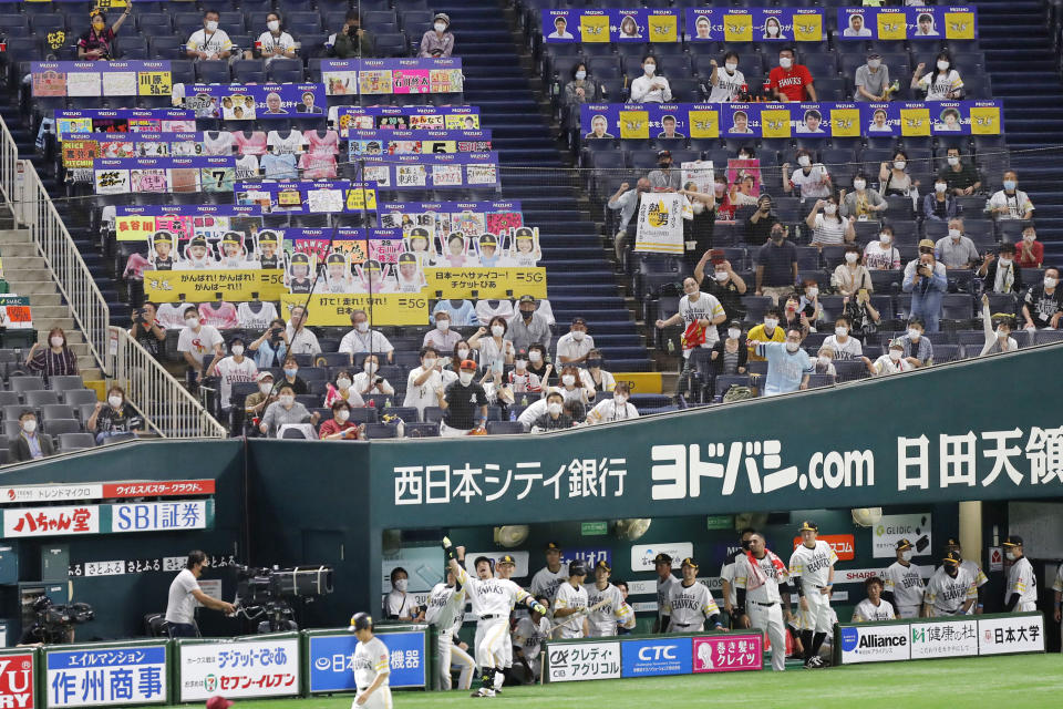 Fans wearing face masks cheer as SoftBank Hawks' Nobuhiro Matsuda, center, celebrates after hitting a solo home run against Rakuten Golden Eagles in the second inning of a regular season baseball game in Fukuoka, southwestern Japan, Friday, July 10, 2020. Japan’s professional baseball league began allowing up to 5,000 fans into the games on Friday, or 50% of the stadium capacity - whichever is smaller. Officials hope to allow the stadiums to be filled to 50% capacity beginning on Aug. 1. (Kyodo News via AP)