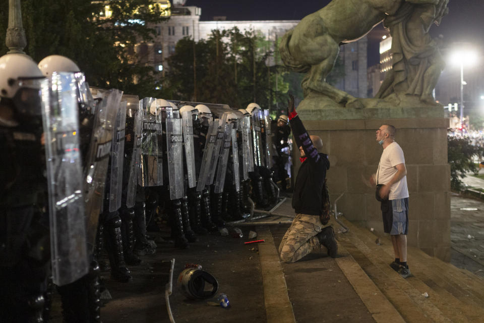 A protester kneels in front of riot police on the steps of the Serbian parliament in Belgrade, Serbia, Friday, July 10, 2020. Hundreds of mostly far right supporters on Friday tried to storm the national parliament in Belgrade, targeting the police for the fourth night of protests against the Serbian president and his rule amid a spike in coronavirus cases in the Balkan country. (AP Photo/Marko Drobnjakovic)