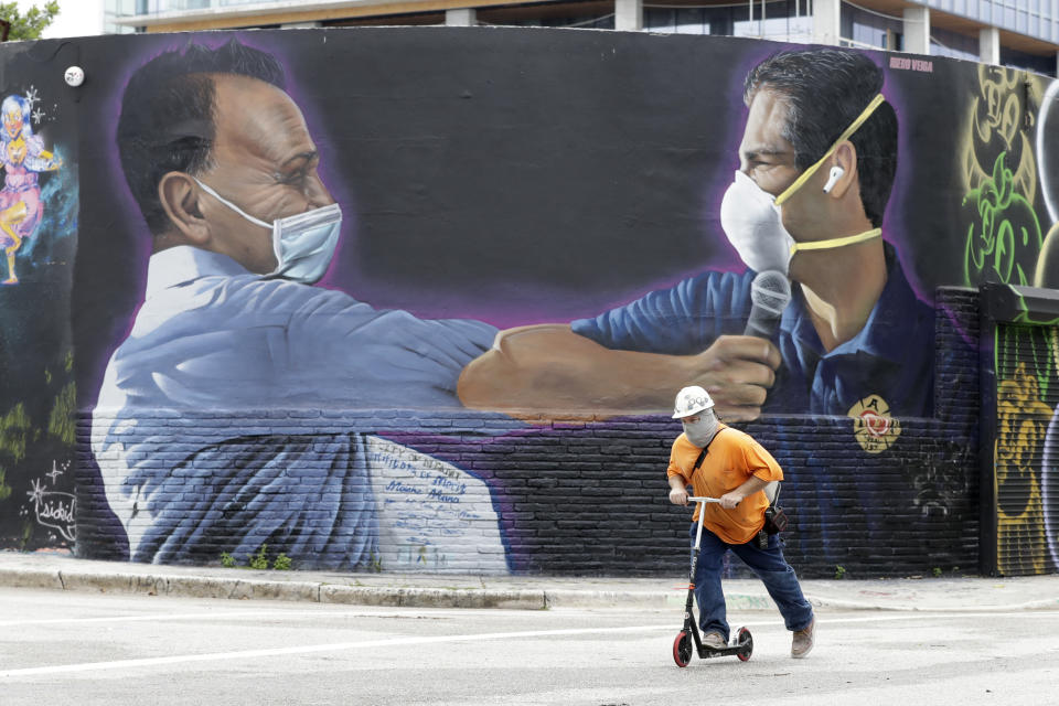 A construction worker rides a scooter past a mural by Hiero Veiga of billionaire businessman Moishe Mana, left, and City of Miami Mayor Francis X. Suarez wearing masks Monday, July 13, 2020, in the Wynwood Arts District of Miami. Florida's rapidly increasing number of coronavirus cases is turning Miami into the "epicenter of the pandemic," a top doctor warned Monday, while an epidemiologist called the region's situation "extremely grave." (AP Photo/Wilfredo Lee)