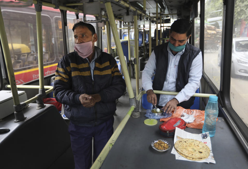 Delhi Transport Corporation bus driver Surinder Singh, 47, left, wearing a face mask as precaution against coronavirus and pollution get ready to eat his lunch at a bus terminal, in New Delhi, India, Wednesday, Nov. 25, 2020. India is grappling with two public health emergencies: critically polluted air and the pandemic. Nowhere is this dual threat more pronounced than in the Indian capital New Delhi, where the spike in winter pollution levels has coincided with a surge of COVID-19 cases. (AP Photo/Manish Swarup)